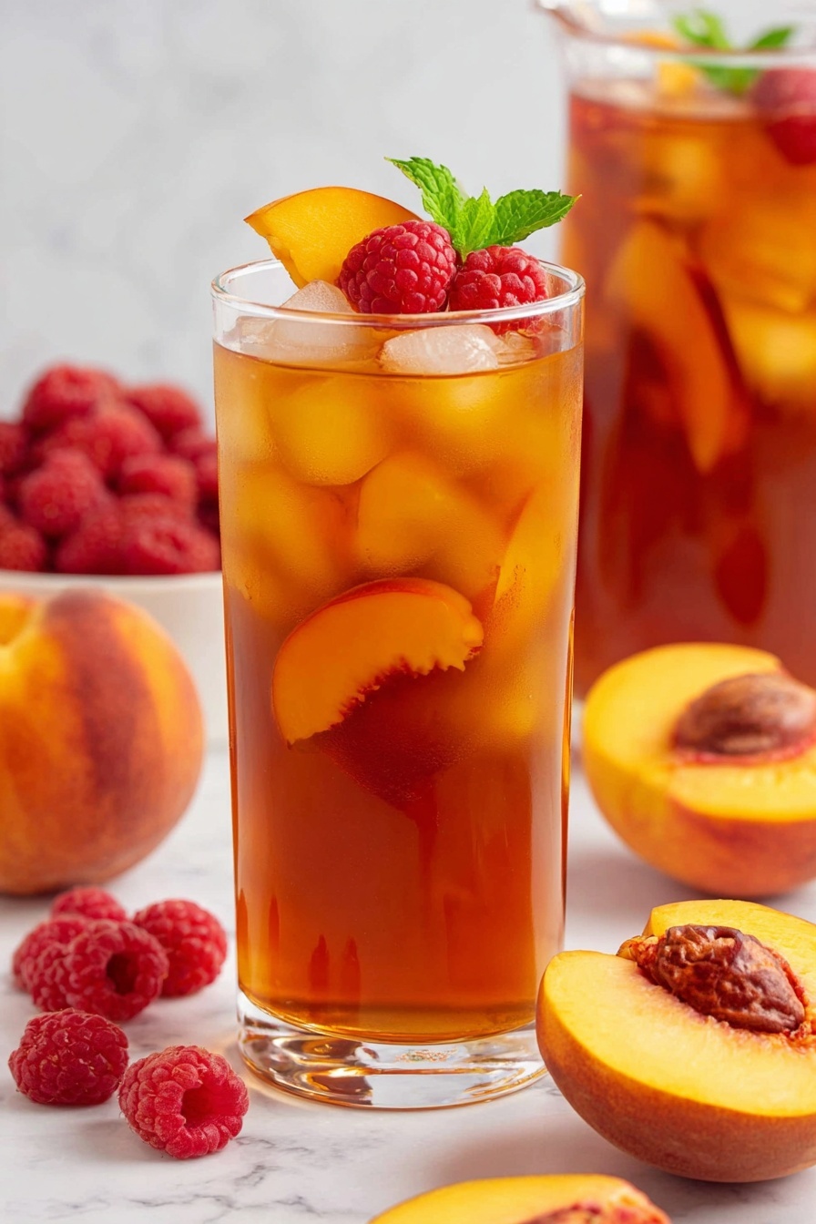 The image shows four tall clear glasses filled with iced peach tea on a white marbled surface. Each glass has amber orange liquid with visible ice cubes that look cold and clear. Inside each glass is a bright yellow-orange peach slice standing out against the dark tea. The front glass has a black straw, and two others have black and white zigzag patterned straws. Each glass is topped with a small green mint leaf for decoration. Around the glasses are whole peaches with soft pink and orange skin and a few fresh green mint leaves adding natural color to the scene. In the background, the blurred pitcher matches the glasses with similar dark tea and ice cubes. Photo taken with an iphone --ar 2:3 --v 7
