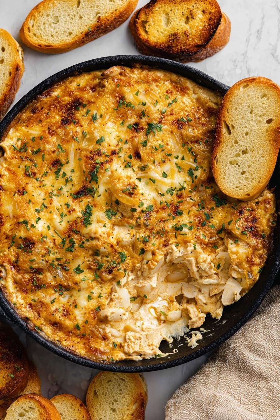 The image shows a round black skillet filled with a thick, creamy dip that has a golden-brown top layer of melted cheese with a slightly crispy texture and scattered bits of herbs. The cheese layer is uneven, revealing a softer, cheesy and chunky inside with visible pieces of onions. Light golden toasted bread slices are placed on the side of the skillet and some are partially dipped into the cheese mixture. The skillet is set on a white marbled surface with extra toasted bread slices scattered around, and the edge of a beige cloth is seen in the corner. photo taken with an iphone --ar 2:3 --v 7