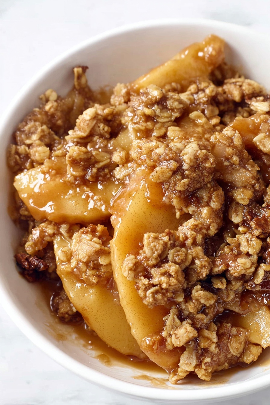 A white bowl is filled with a rich apple crisp dessert showing several layers of soft cooked apple slices with a warm golden-brown color, covered by a thick crumbly topping that has a rough texture with visible oats and nuts. The dessert is coated in a shiny, sticky caramel-like sauce, adding a glossy look to the tender fruit and crunchy topping. The apple slices are slightly translucent and tender, nestled closely together beneath the crisp topping. The white bowl is set on a white marbled surface, enhancing the warm tones of the dessert. photo taken with an iphone --ar 2:3 --v 7