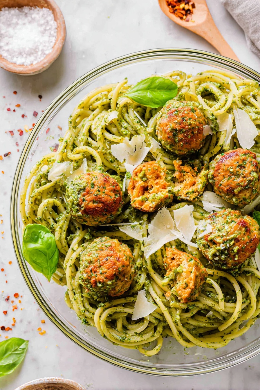 A white bowl filled with thick spaghetti coated in green pesto sauce, twisting around a golden fork with a black handle at the left side. On top of the spaghetti, there are seven round meatballs with a slightly browned outside and bits of green and orange herbs and vegetables inside. Two meatballs are cut open to show the inside texture. Thin, flat slices of pale cheese and small green basil leaves are scattered on the pasta. The bowl rests on a white marbled surface. photo taken with an iphone --ar 2:3 --v 7