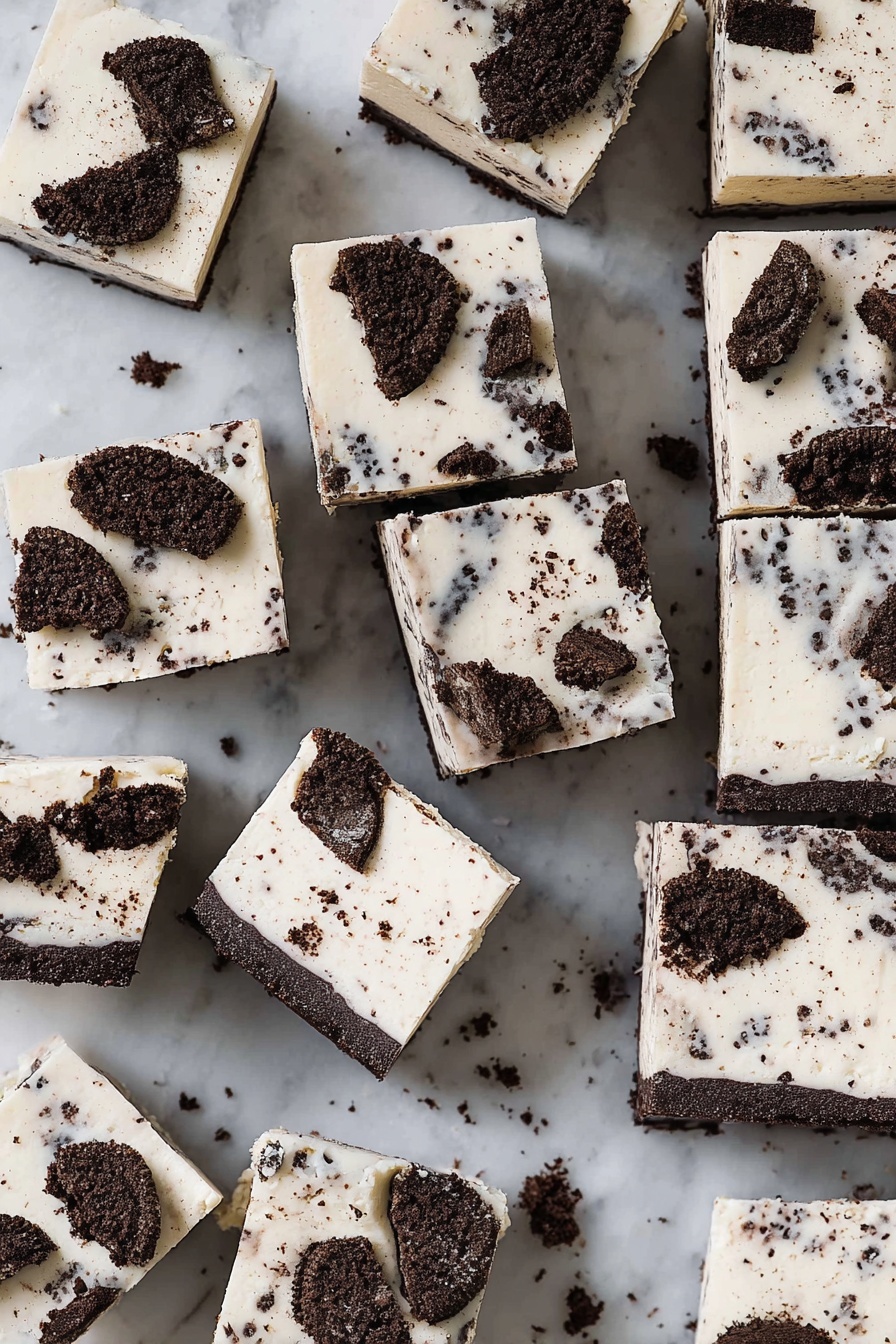 The image shows many square pieces of a white layered dessert with dark cookie chunks mixed and on top. Each piece has a thick white top layer with small dark cookie specks inside it, and larger cookie chunks placed on the surface. The bottom layer appears darker, likely the cookie base, contrasting with the smooth white top. The pieces are placed randomly on a white marbled surface, with some crumbs scattered around. Photo taken with an iphone --ar 2:3 --v 7