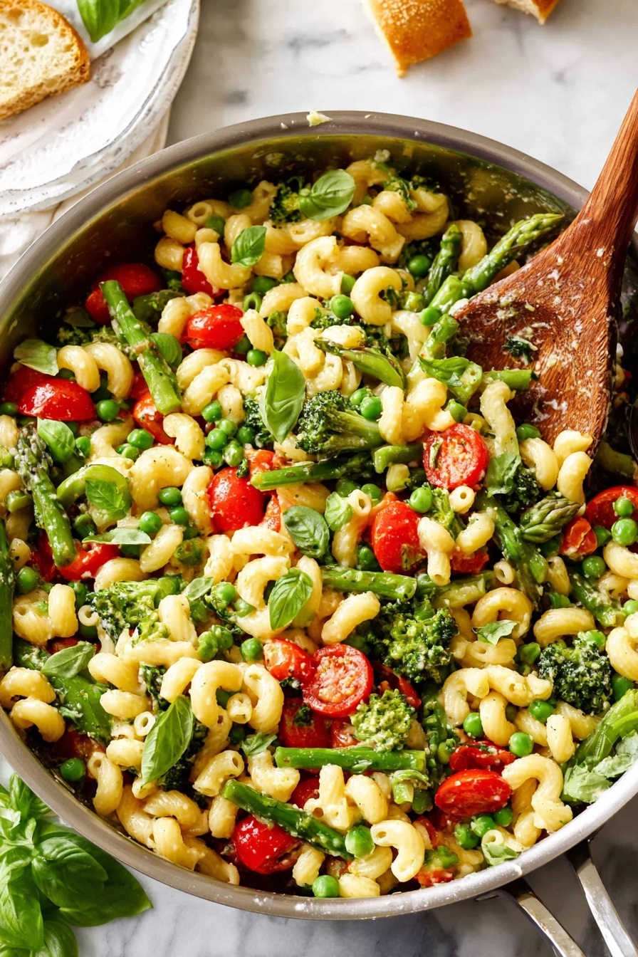 The image shows a large metal pan filled with pasta shaped like small curly tubes, mixed with green broccoli florets, bright green peas, cut red cherry tomatoes, and pieces of green asparagus. Fresh green basil leaves are scattered on top, adding a pop of color. A wooden spoon rests inside the pan, partially covered by the pasta mix. The pan is placed on a white marbled surface, and in the background, a white plate with bread is partly visible. The overall look is fresh, colorful, and vibrant, with a mix of smooth pasta and crisp vegetable textures. photo taken with an iphone --ar 2:3 --v 7