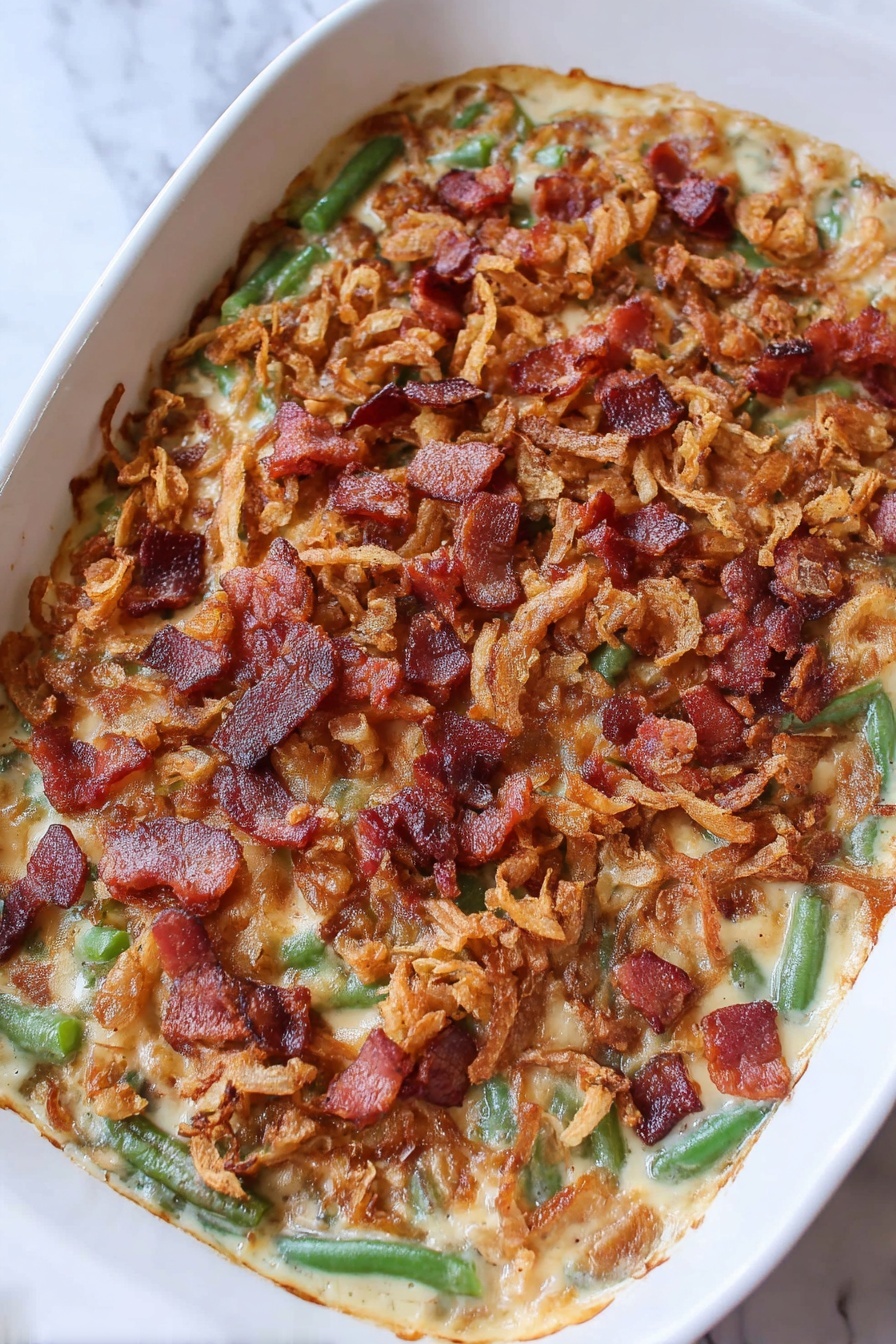 The image shows a baked casserole in a white dish, filled with a creamy base mixed with green beans visible throughout. The top is covered with golden brown crispy fried onions spread evenly, and small chunks of crispy, reddish-brown cooked bacon scattered all over. The casserole surface has a textured, slightly bubbly look with the topping layer crisply contrasting with the creamy and green base underneath. The dish sits on a white marbled surface. photo taken with an iphone --ar 2:3 --v 7
