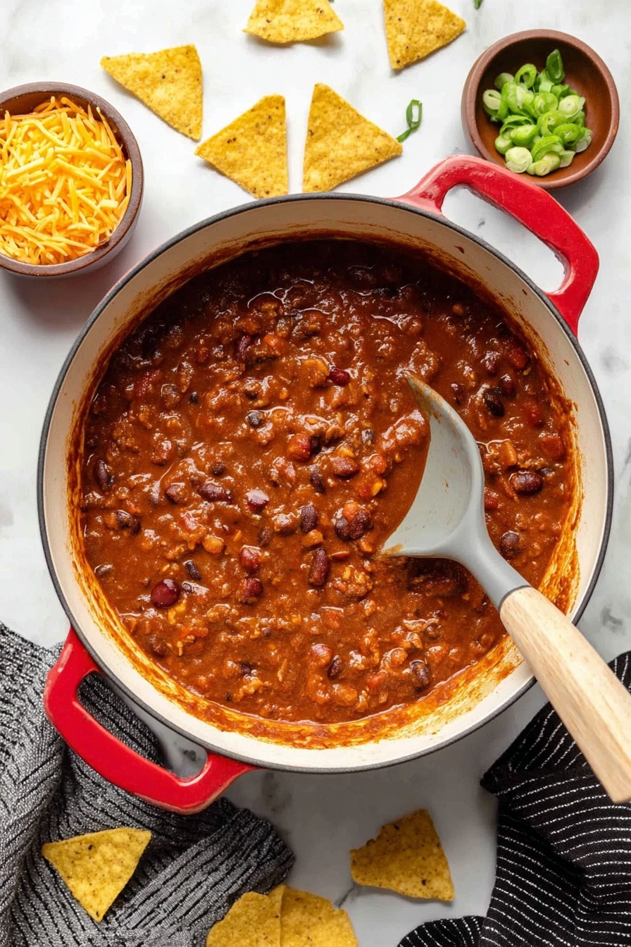 A large white enamel pot with red handles filled with thick, chunky chili that has a deep reddish-brown sauce mixed with beans and pieces of meat, with a gray spoon with a light wooden handle resting inside the pot. On the white marbled surface around the pot are scattered yellow tortilla chips, a small brown bowl with chopped green onions, and another small brown bowl with shredded yellow cheese. A black and white striped cloth is partially visible under the pot. Photo taken with an iphone --ar 2:3 --v 7