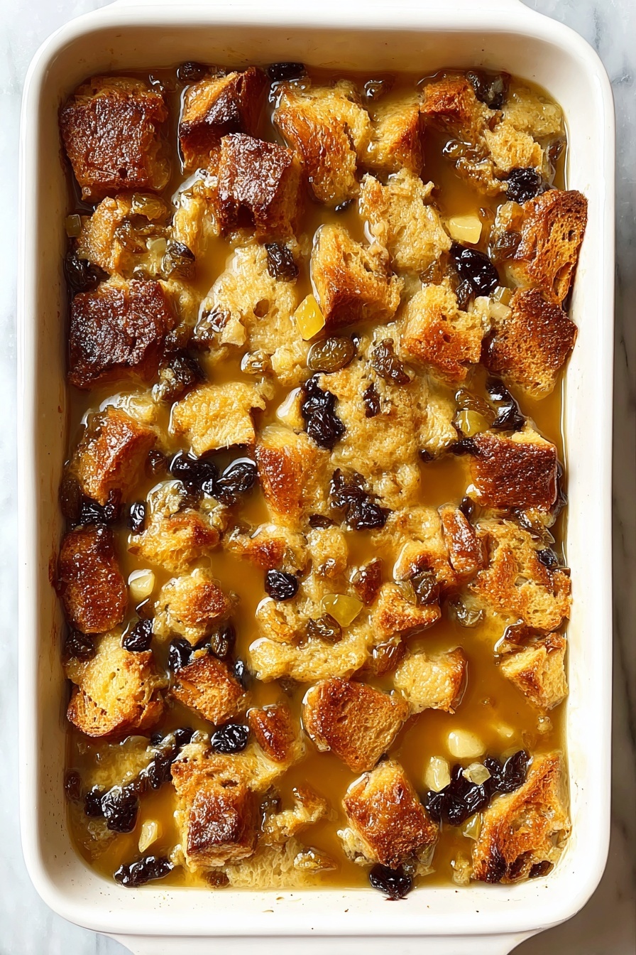 This image shows a close-up of a golden metal serving spoon lifting a portion of bread pudding from a white baking dish. The bread pudding has three main layers: a top crust that is slightly crispy and golden brown, a middle layer with soft, chunky bread pieces in light brown color, and dark brown raisins scattered throughout. A glossy, light caramel sauce is drizzled over the top, giving the bread pudding a sticky and moist look. The white baking dish sits on a white marbled texture surface. The photo taken with an iphone --ar 2:3 --v 7