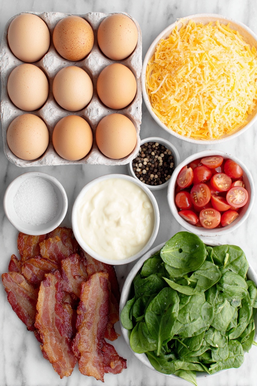 Flat lay of eighteen whole uncracked brown eggs, a small white ceramic bowl of creamy half and half, a small white ceramic bowl of coarse salt, a small white ceramic bowl of whole black peppercorns, a simple white plate piled with bright orange grated sharp cheddar cheese, a small white ceramic bowl of fresh baby spinach leaves, a small white ceramic bowl of halved glossy red grape tomatoes, a small white ceramic bowl of cooked crispy chopped bacon lined with golden edges, all arranged symmetrically and balanced, placed on a clean white marble surface, soft natural light, photo taken with an iPhone, professional food photography style, fresh ingredients, white ceramic bowls, no bottles, no duplicates, no utensils, no packaging --ar 2:3 --v 7 --p m7354615311229779997
