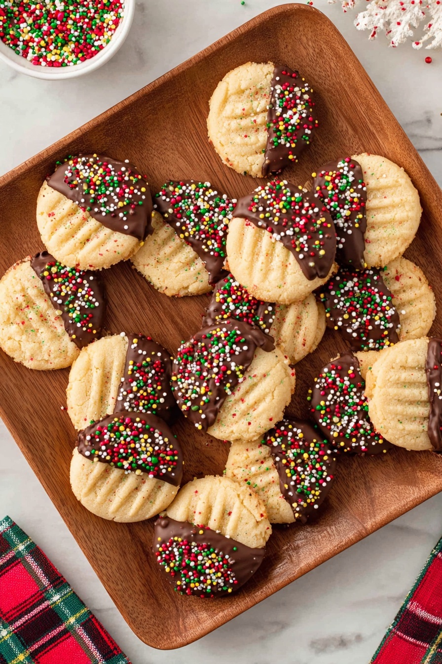 The image shows a wooden square plate filled with ten round cookies arranged randomly. Each cookie is half dipped in dark brown chocolate on one side, topped with colorful festive sprinkles in red, green, yellow, and white. The cookies have a light golden brown color with a slightly crisscross textured surface on the plain side. The plate sits on a white marbled surface, and there is a plaid cloth with red, green, and white colors at the bottom right corner of the image. Photo taken with an iphone --ar 2:3 --v 7