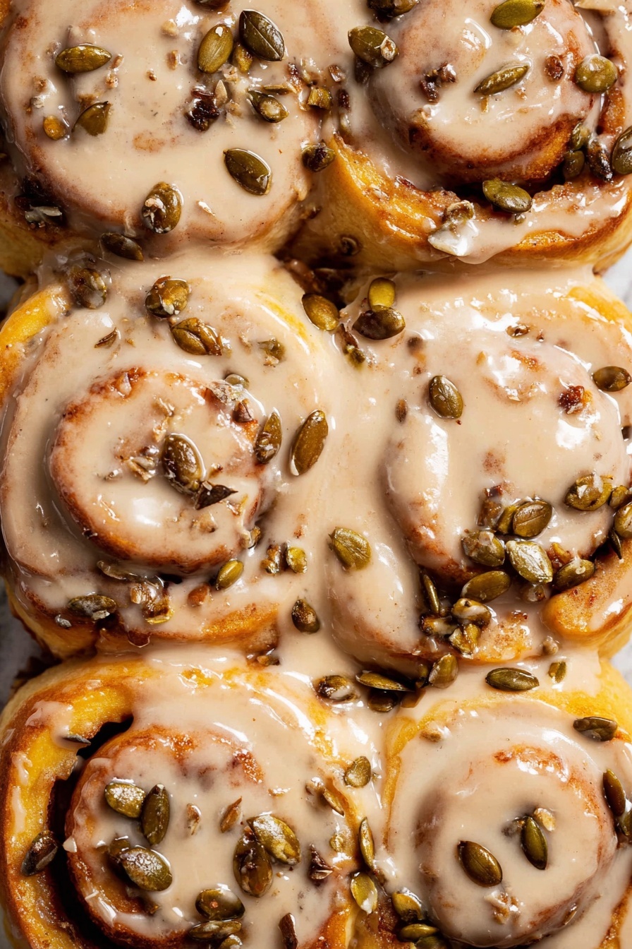 The image shows close-up pieces of cinnamon rolls with a golden-brown baked texture, where one piece is pulled apart showing soft, chewy layers inside matching the warm brown cinnamon color. Each roll is covered with a creamy beige icing dripping over the edges, and some chunks of nuts are visible on top adding rough texture. The rolls sit on a white marbled surface with some glaze pooling around them, creating a cozy and warm feel. Photo taken with an iphone --ar 2:3 --v 7