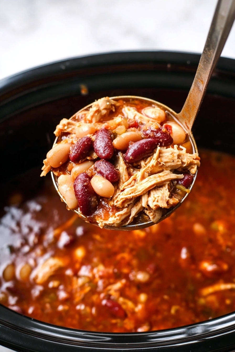 The image shows a white bowl filled with a brownish-red soup that has visible pieces of shredded chicken and kidney beans in it. On top, there are bright yellow shredded cheese and crushed tortilla chips, fresh green chopped scallions, and a sliced round green jalapeño pepper. The soup looks thick and hearty with shiny, moist textures. A vintage silver spoon with a detailed handle rests inside the bowl. The bowl sits on a white marbled surface with some scattered tortilla chips pieces around. The photo taken with an iphone --ar 2:3 --v 7