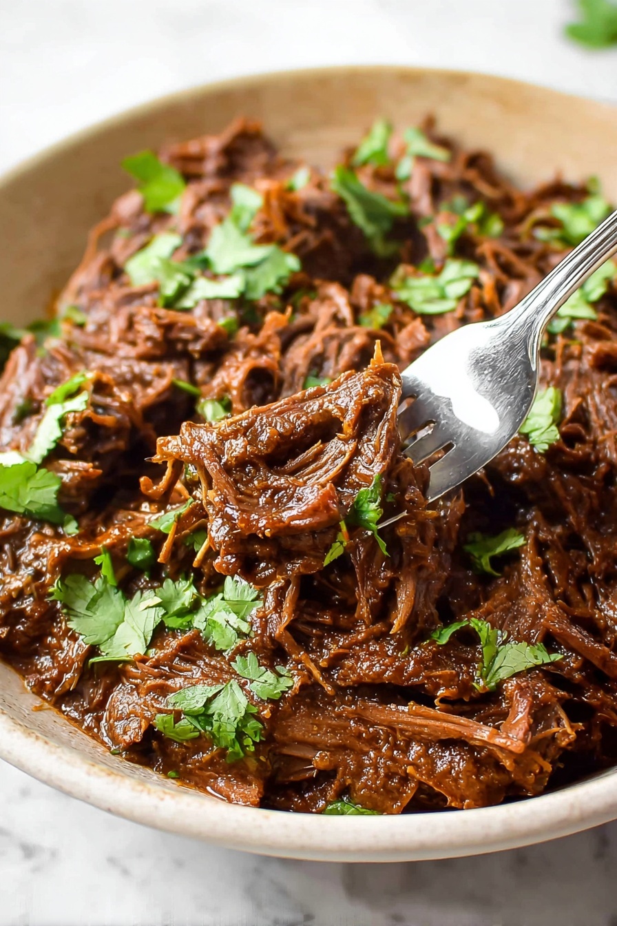 The image shows a shallow white bowl filled with shredded, dark brown beef cooked in a rich sauce. The beef pieces have a moist, tender texture with some stringy strands visible, mixed evenly throughout the dish. Bright green cilantro leaves are scattered on top for a fresh contrast. A silver fork holds a small amount of the beef close to the bowl, and the bowl rests on a white marbled surface. The lighting gives the beef a slight shine, highlighting its juicy texture. photo taken with an iphone --ar 2:3 --v 7