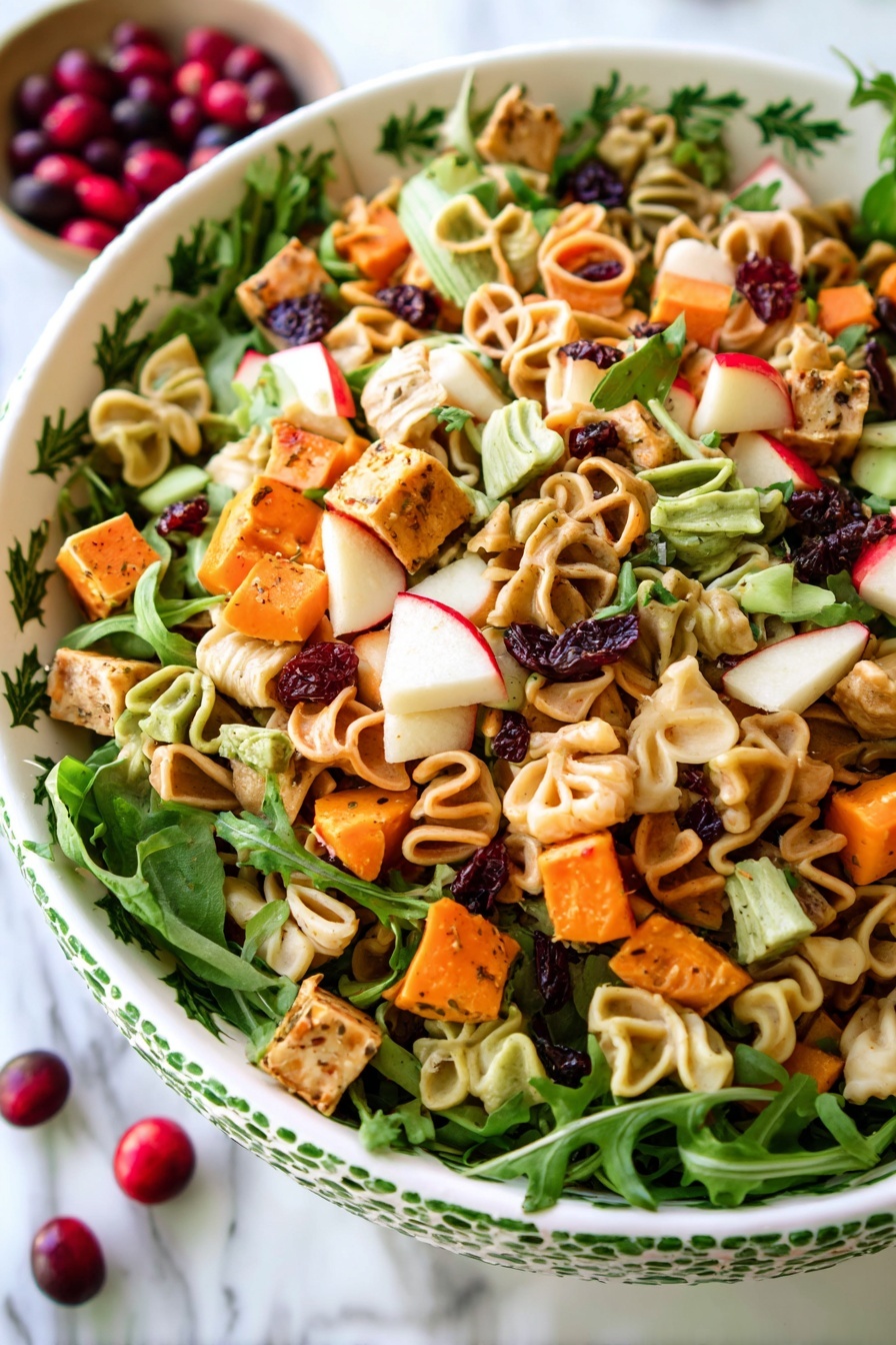 A close-up view of a colorful pasta salad served in a white bowl with green holly leaf patterns on the rim. The salad has three layers: the bottom layer is shaped pasta in beige, tan, and green colors with pumpkin and tree patterns; the middle layer contains small cubes of orange sweet potato, red apple, and white cheese; the top layer is fresh green arugula leaves scattered throughout, along with small dark red dried cranberries. The bowl sits on a white marbled surface with a few whole red cranberries placed nearby. Photo taken with an iphone --ar 2:3 --v 7