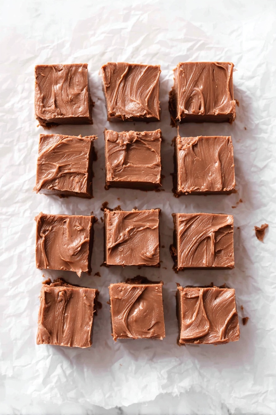The image shows sixteen square pieces of chocolate fudge arranged in four rows and four columns on crinkled white parchment paper placed on a white marbled surface. Each fudge piece has a smooth, creamy texture with some swirled and uneven marks on top. The chocolate color is rich and deep, with slight variations in shade across the squares, giving a homemade feel. The pieces are evenly spaced with some small crumbs and soft edges visible around them, suggesting they were freshly cut. photo taken with an iphone --ar 2:3 --v 7