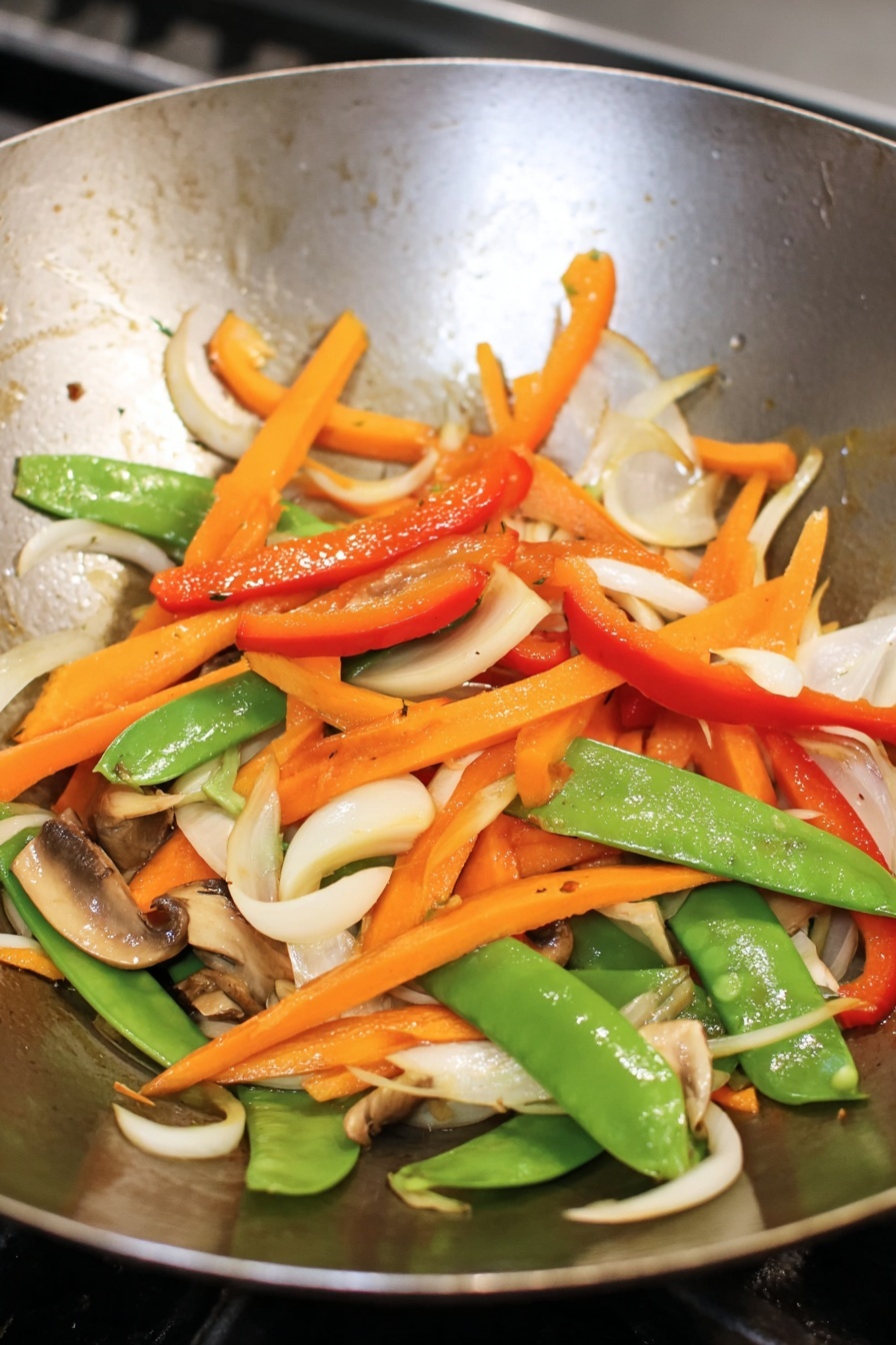 The image shows a large white plate full of stir-fried noodles mixed with colorful vegetables and pieces of cooked chicken. The bottom layer consists of thick, golden-brown noodles twisted around each other. Scattered on top are bright green snap peas, thin red and orange carrot strips, and green onion pieces, plus small chunks of cooked chicken with a light brown color. The dish is sprinkled with white sesame seeds and chopped green onions. Around the plate, there are fresh mushrooms, garlic bulbs, garlic cloves, and green onions on a white marbled surface. photo taken with an iphone --ar 2:3 --v 7