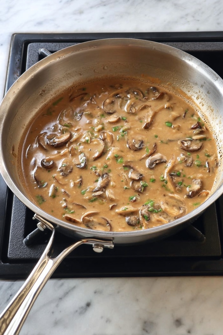 A white round plate holds a meal with three main parts. On the left side, there is a bundle of bright green asparagus standing upright with a slight shine. In the middle, a golden brown cooked chicken piece is topped with several slices of brown mushrooms covered in a light brown sauce sprinkled with small green herb bits. On the right side, there is a large serving of creamy white mashed potatoes topped with the same brown mushroom sauce and mushroom slices, also with green herb bits sprinkled on top. The plate rests on a white marbled surface. Photo taken with an iphone --ar 2:3 --v 7