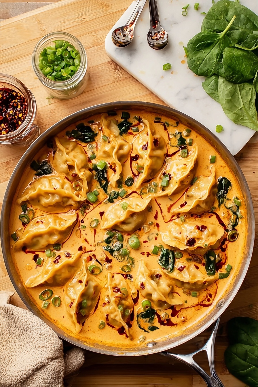 A round skillet filled with a creamy orange sauce holding nine golden dumplings spread evenly around, each dumpling folded in a semi-circle with a lightly browned texture. Swirls of dark red chili oil and scattered chopped green onions sit on top and in the sauce, with some spinach leaves partially covered by the sauce. On the side, fresh green spinach leaves, a white cutting board with chopped green onions, a glass jar with spoon inside containing chili oil, and metal measuring spoons rest on a wooden surface that is changed to a white marbled texture. A beige oven mitt is placed near the skillet. photo taken with an iphone --ar 2:3 --v 7